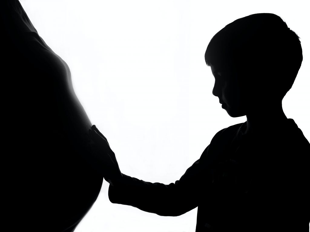 Boy with hand on pregnant womans stomach, both in silhouette.